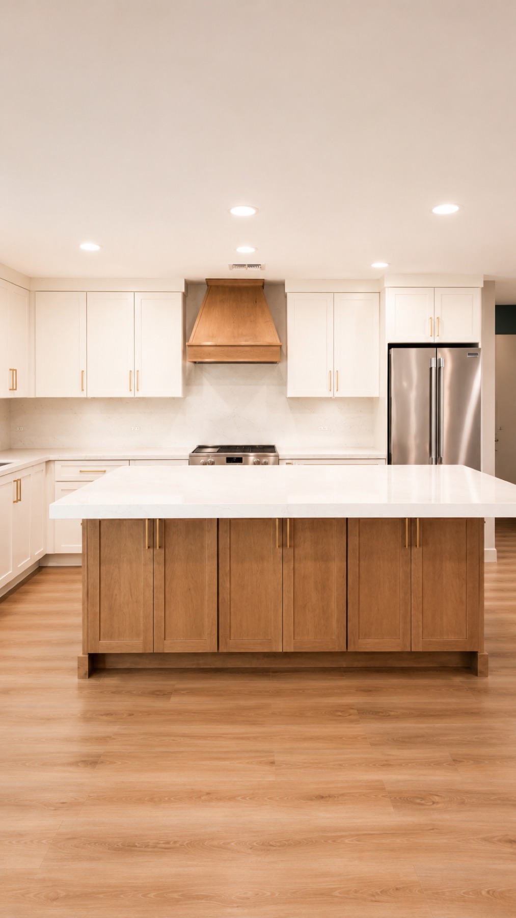 New kitchen island in white oak with a thick quartz countertop, flanked by white shaker cabinets and a custom wood range hood