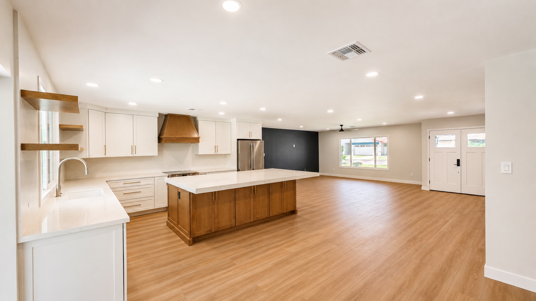 Remodeled open-concept kitchen and living room with a white oak island, custom hood, and light wood-look flooring running to the new front door