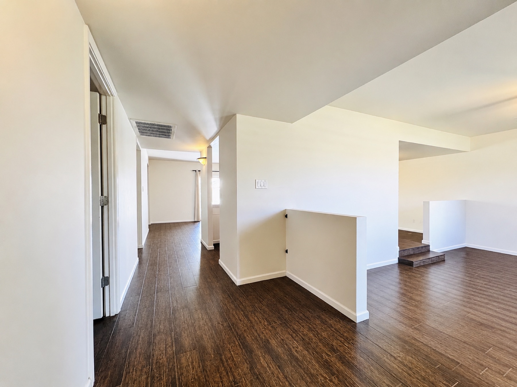 Original entry hallway before the remodel with dark flooring, a half wall, and a narrow corridor to the bedrooms