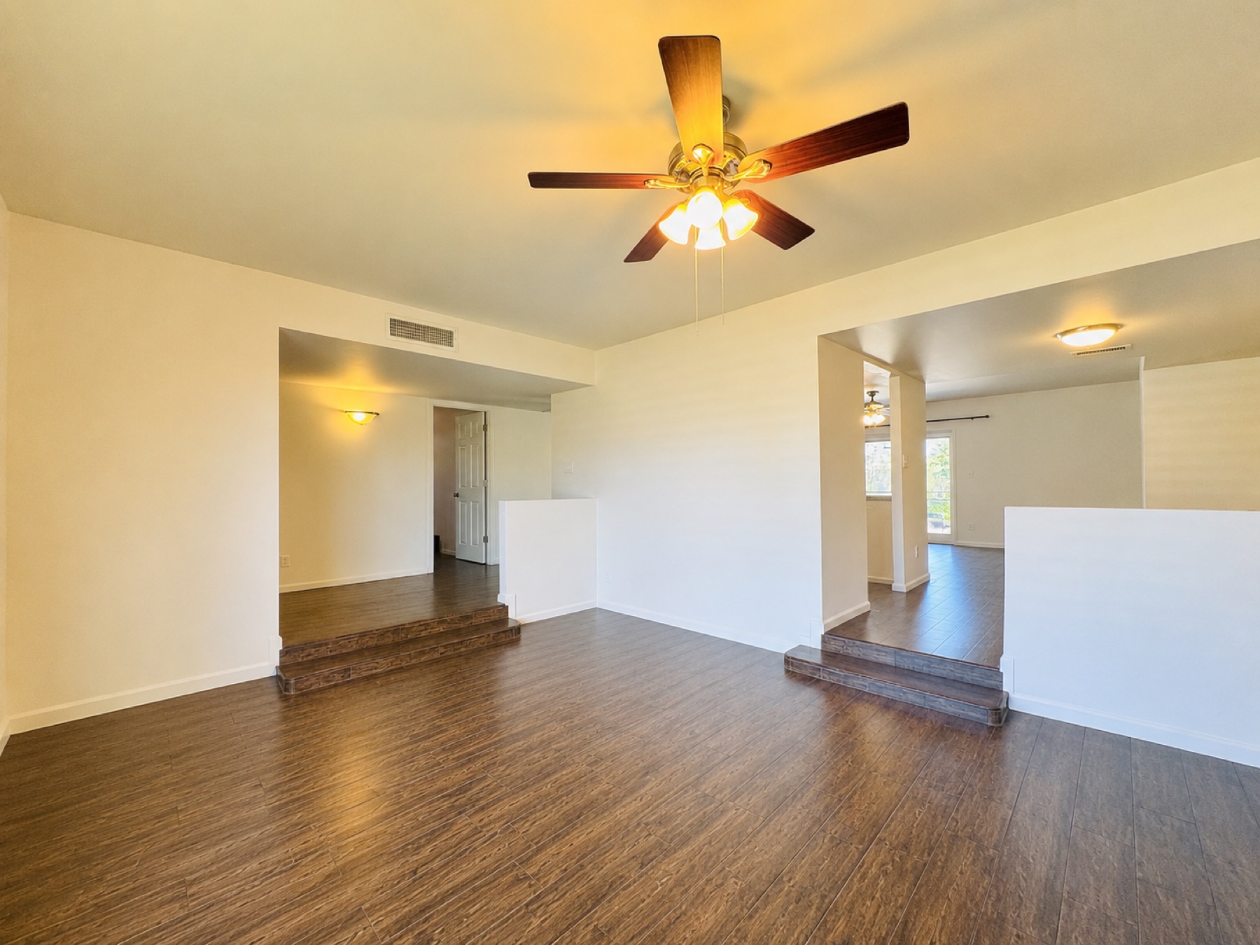 Original sunken living room before the remodel with a dated ceiling fan, dark flooring, and step-down transitions