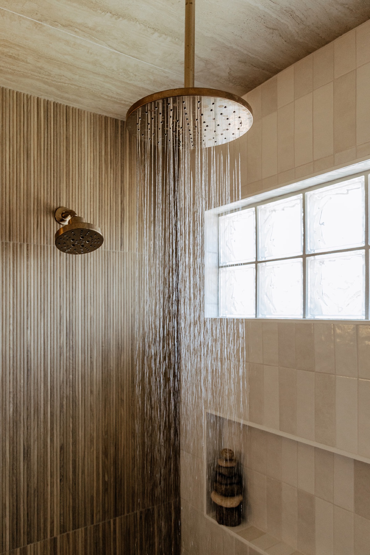 Rainfall shower head running in the new walk-in shower, with a handheld wand and reeded tile wall