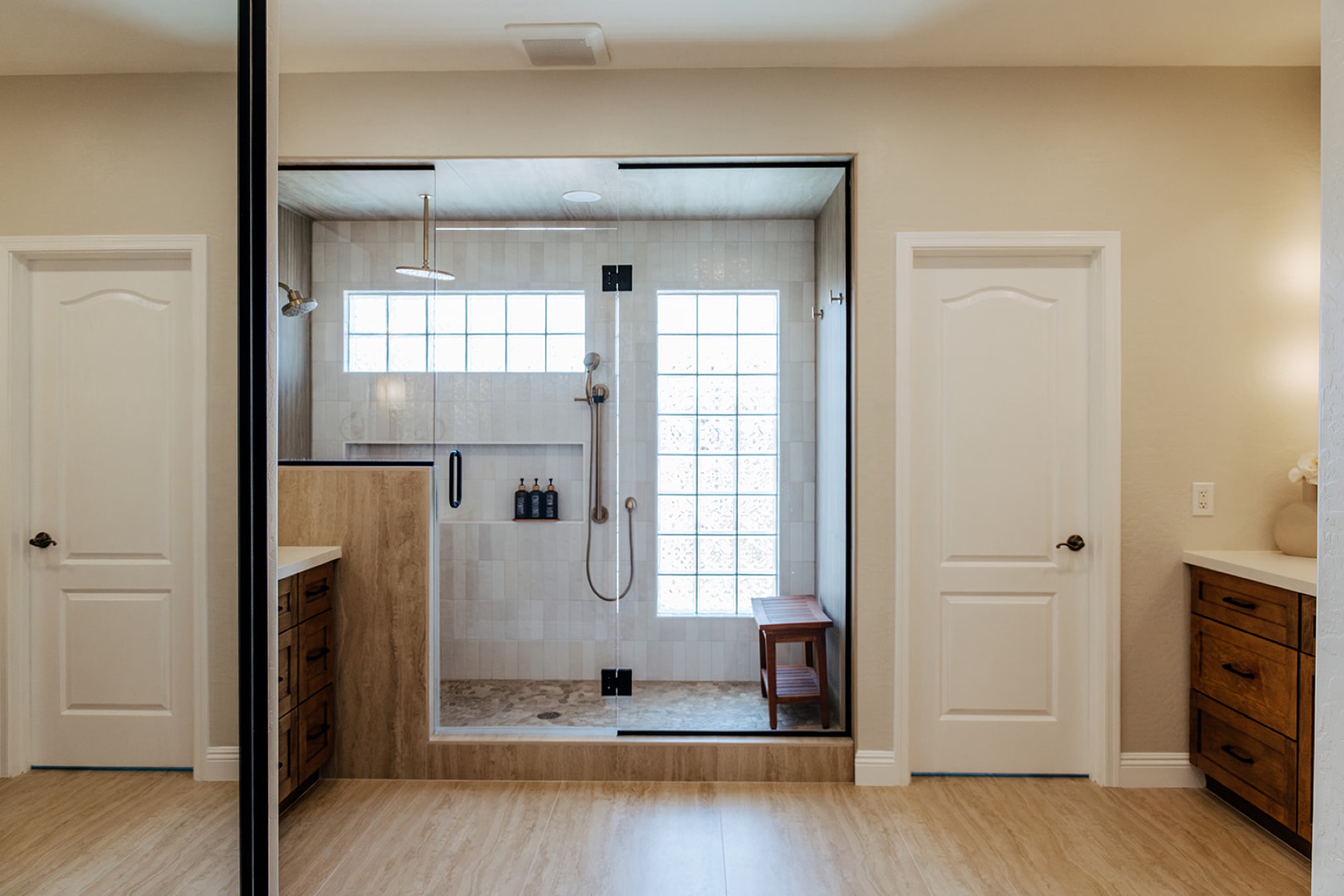 Remodeled walk-in shower with reeded wood-look tile, a glass block window, and a teak bench, framed by the primary bathroom's two entry doors