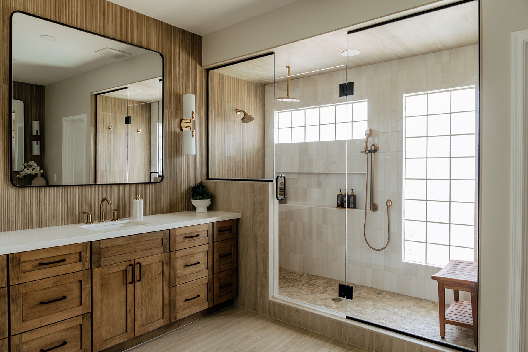Primary bathroom with fluted tile, a warm wood vanity, and brass fixtures